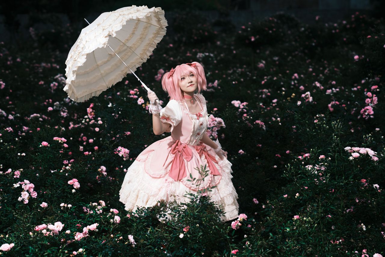 about-us Woman in costume holding a parasol, surrounded by blooming pink flowers.