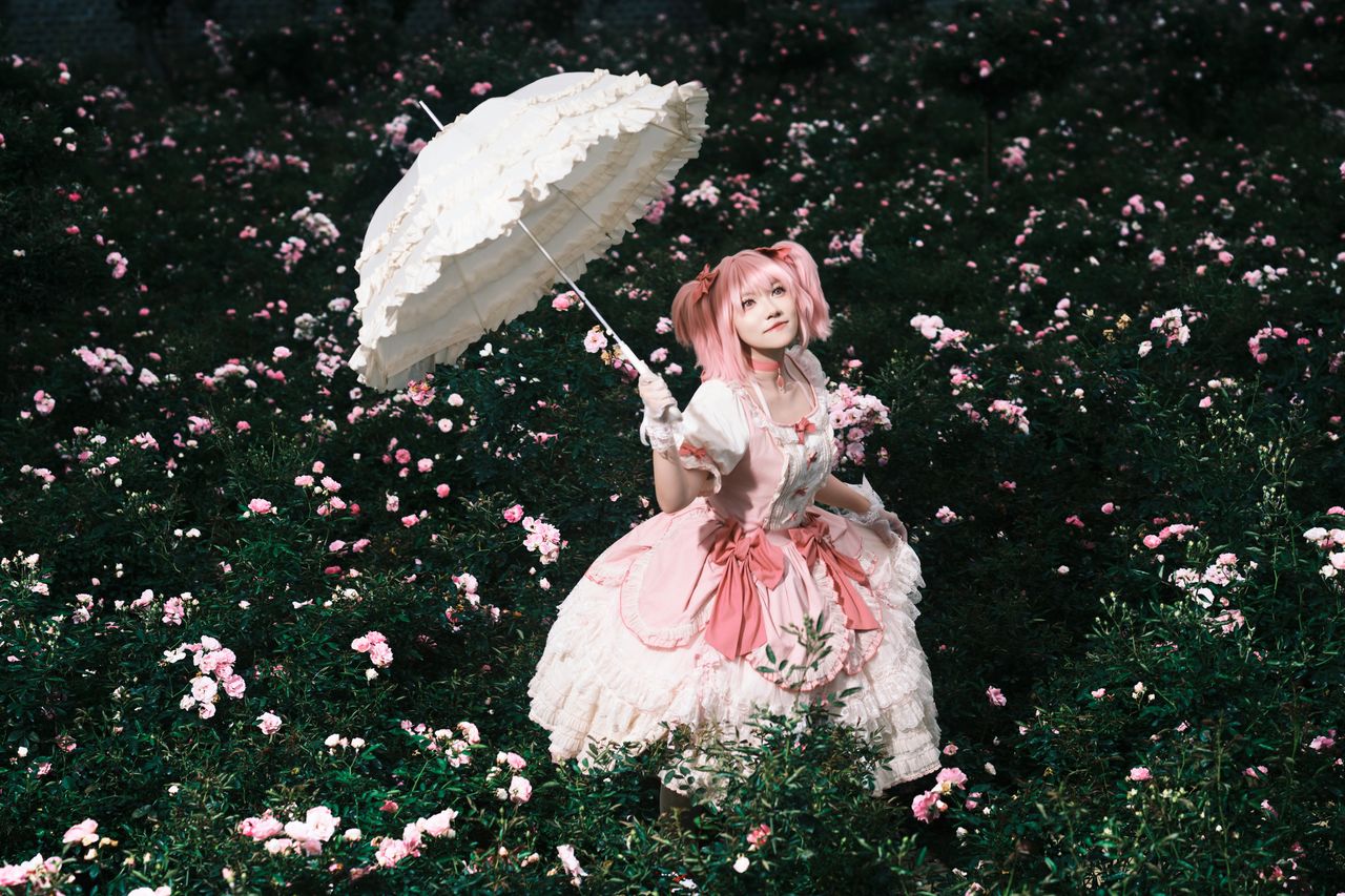 services-03 A person in cosplay holds a parasol, surrounded by vibrant pink flowers in a serene outdoor garden.
