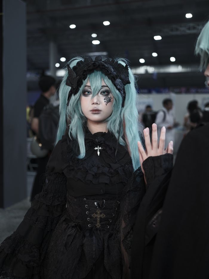 services-02 A person in Gothic Lolita cosplay with turquoise hair at a crowded indoor convention.